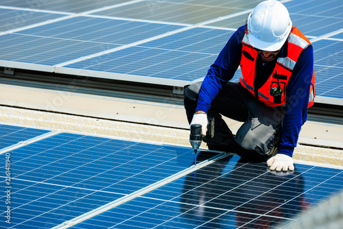 Obraz na plátne Solar technician using a power drill to install and maintain photovoltaic panels on a rooftop, representing renewable energy, skilled engineering, clean electricity and workplace safety
