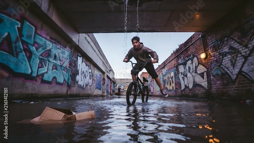 Young Man Riding Bicycle Through Urban Canal with Street Art Surrounding
