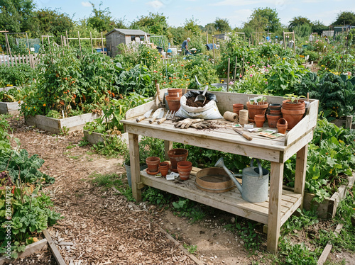 Weathered wooden potting table with terracotta pots gardening tools and watering can in allotment