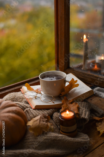 Bild auf Leinwand Cozy Fall Scene with Steaming Mug, Open Book, Pumpkin, and Burning Candle