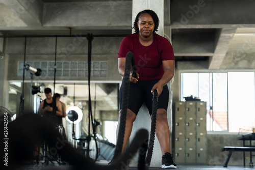Fotografía Plus size African American woman doing intense battle rope workout in modern gym, fitness lifestyle photo for strength cardio training, healthy routine, endurance and body confidence motivation