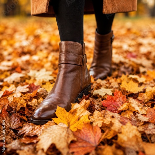 Brown leather boots walking through colorful fallen leaves during the autumn season outdoors