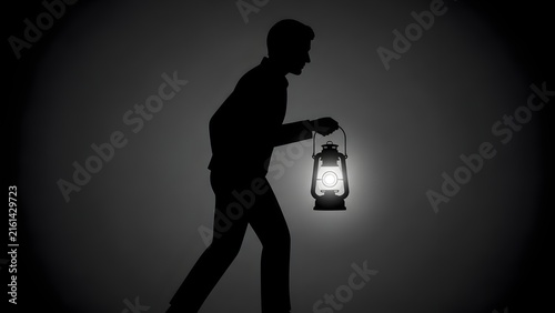 Curious young man walking while holding glowing lantern in darkness