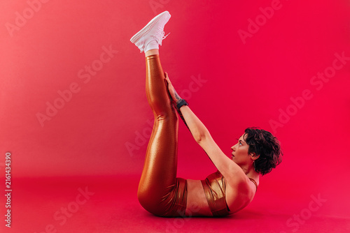 Woman in golden sportswear doing abs exercises while lying in a studio