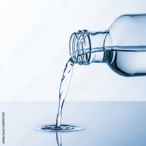 Clear Water Pouring from Glass Bottle onto Reflective Surface.