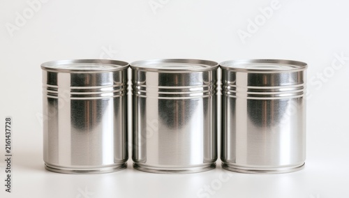 Three identical silver metal tin cans lined up in a row on a white surface.