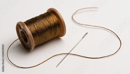 Close-up of a wooden spool of metallic thread with a needle and loose thread.