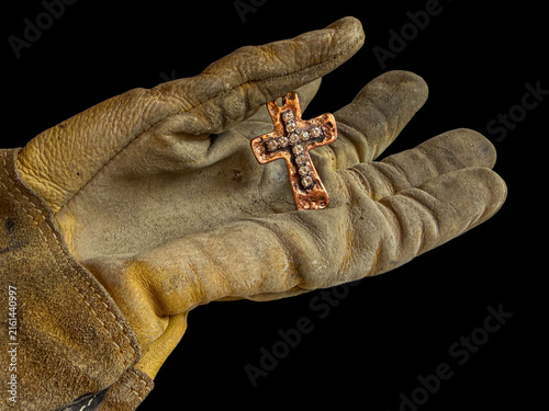 Worker’s leather glove holds saving metal Christian cross with rhinestones indicating salvation for all. Jesus meets you wherever  you work and live. The cross comes to everyone.