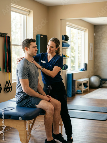 Physical therapist treating male patient in modern rehabilitation clinic with exercise equipment