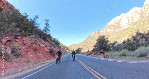 Scenic spring morning e-bike ride through Zion National Park in Utah, USA. Cyclists pedal along dramatic red rock canyons and green trails under soft morning light in this stunning national park lands