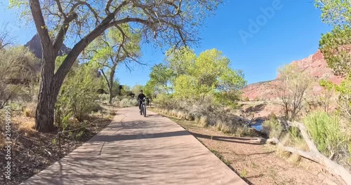 Scenic spring morning e-bike ride through Zion National Park in Utah, USA. Cyclists pedal along dramatic red rock canyons and green trails under soft morning light in this stunning national park lands