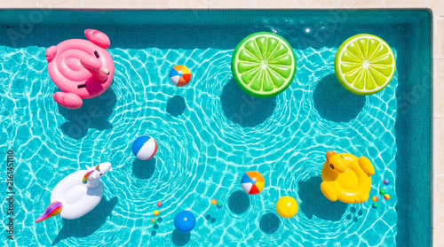 Top down view of colorful inflatable pool floats and beach balls floating in turquoise swimming pool water
