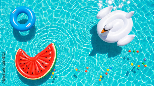 Top down view of colorful inflatable pool floats and beach balls floating in turquoise swimming pool water