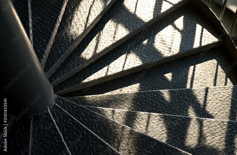 Naklejka premium Industrial spiral staircase with diamond plate treads and patterned shadows