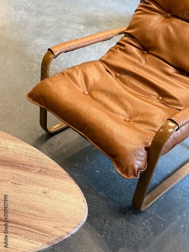 Cafe lifestyle photo of an empty brown leather armchair and part of a simple table. Minimal cafe interior scene with cozy seating and no people