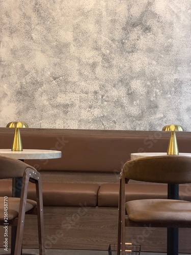 Empty cafe interior with two tables, chairs, brown seating, and a plain empty wall. Vertical lifestyle photo in a cozy restaurant atmosphere. Cafe interior, minimalist style and no people
