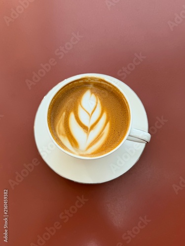 cup of coffee. cappuccino coffee cup on a saucer, white ceramic cup isolated. Top view of latte art, dark red table background