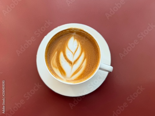 Cappuccino coffee cup on a saucer. Cafe scene, white ceramic cup, latte art, dark red table background. Isolated coffee cup, horizontal view
