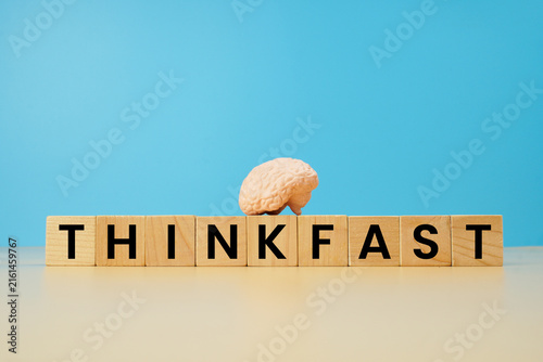 Think fast concept with wooden letter blocks and miniature human brain model on blue background, representing quick thinking, intelligence, decision making and cognitive skills.