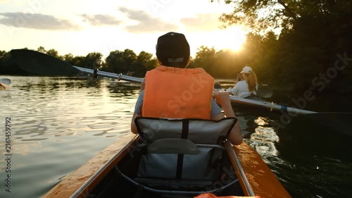 Back view of child in life jacket kayaking on lake during golden hour sunset.