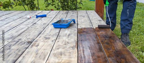 Person applies dark wood stain to weathered wooden deck planks