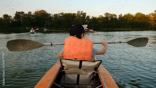 Back view of people kayaking on a calm river during summer sunset.