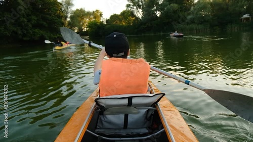 Back view of people kayaking on a calm river during summer sunset.