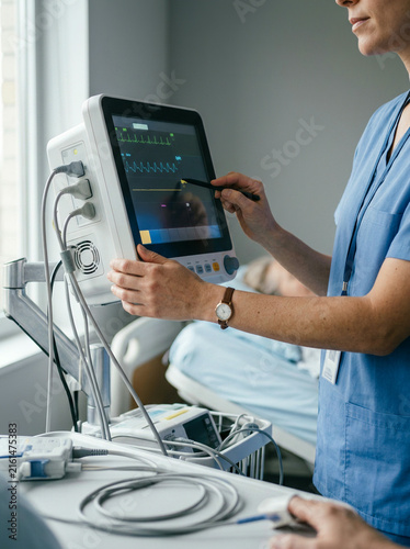 Clinician in blue scrubs using a stylus on a bedside heart monitor screen