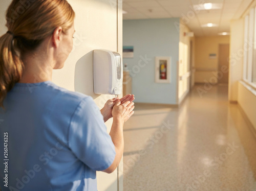 Healthcare worker dispensing sanitizer from a wall mounted dispenser indoors