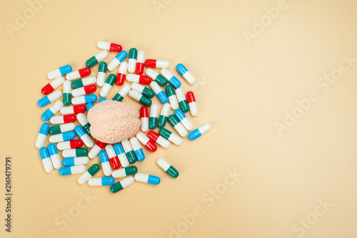 Human brain model surrounded by colorful capsules on yellow background, representing brain medication, mental health treatment, neurology, pharmacy and healthcare.