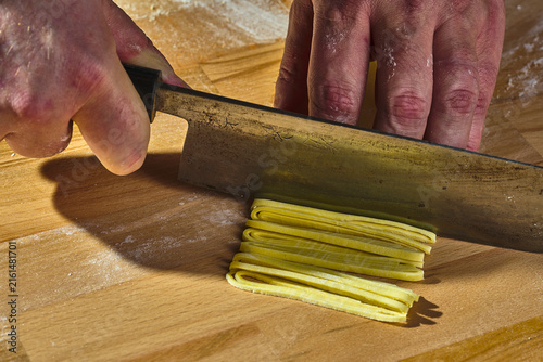 Hands cutting fresh pasta dough on wooden board