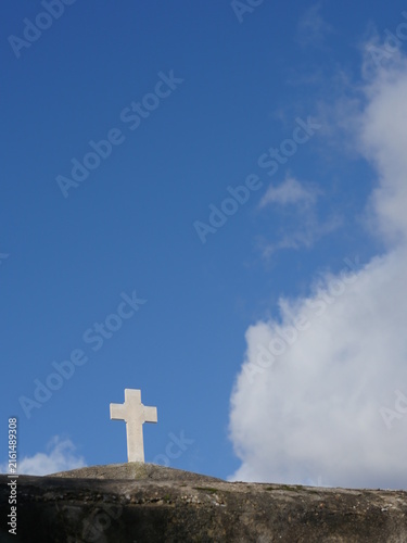 White cross is on a hilltop in front of a blue sky