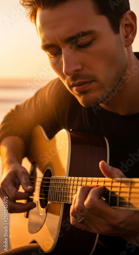 Close up portrait of handsome man playing acoustic guitar with eyes closed during golden sunset light