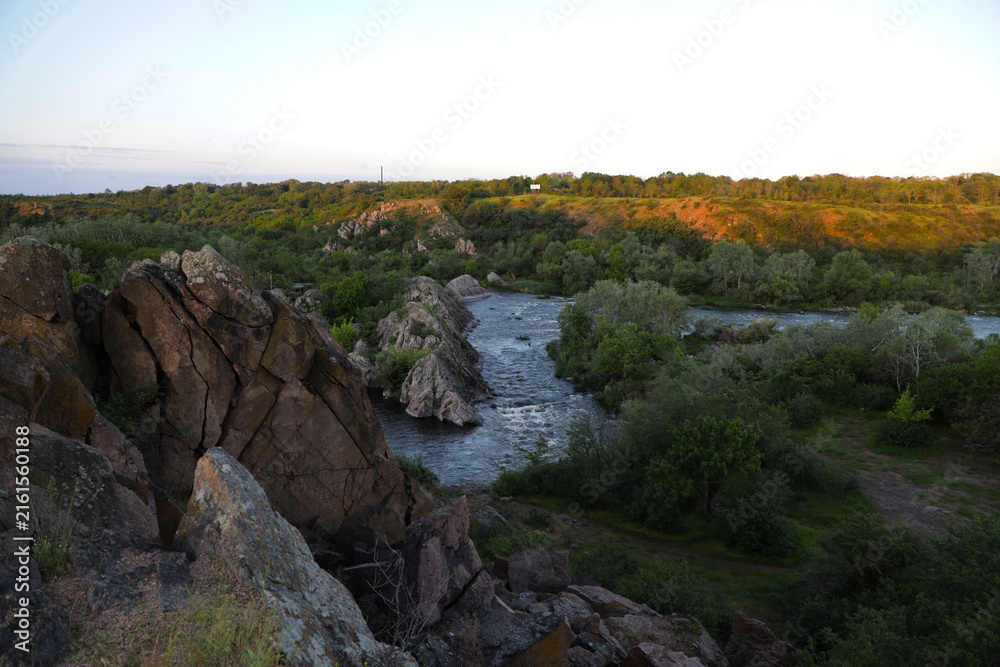 Fototapeta premium Scenic summer landscape of a fast mountain river rushing over rocks with green grassy cliffs