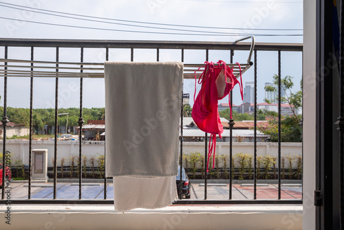 Towel and women's swimsuit drying on a balcony rack. Everyday laundry care with city view, sunlight, outdoor living, and summer vacation concept.
