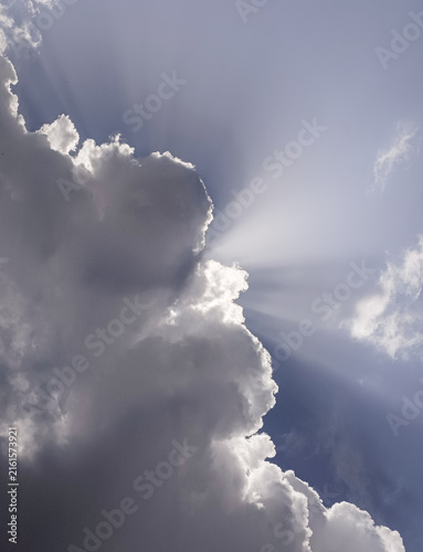 Foto A vertical shot of powerful sun rays bursting from behind a massive fluffy cloud