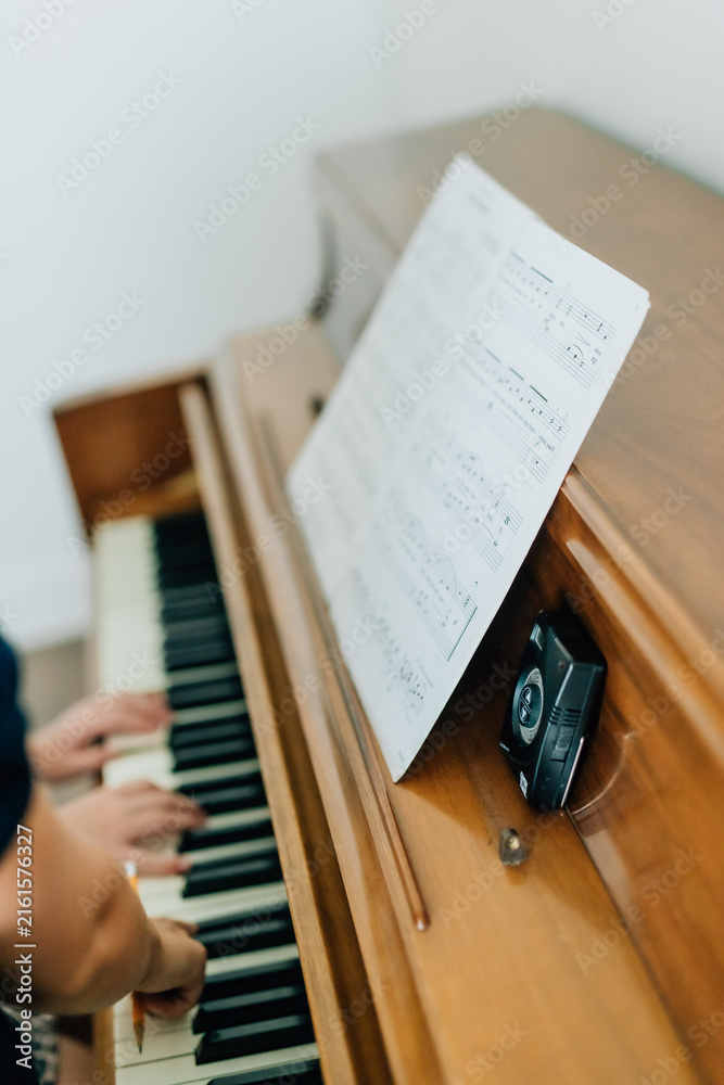 Obraz premium childs hands playing on piano keys with sheet music and metronome