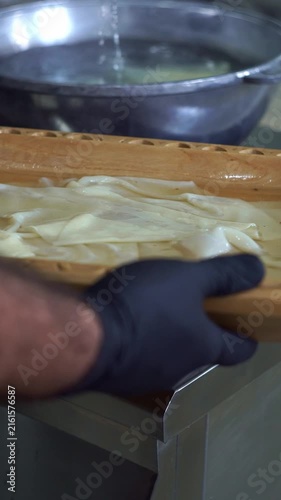 Chef in black gloves holding a wooden platter filled with freshly boiled dough sheets for beshbarmak