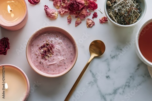 Close up flat lay of a luxurious self care ritual with face mask, rose petals, candle, and herbal tea on white marble, showing how people unwind through relaxing wellness routines home