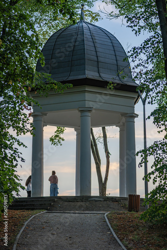 Cuadro en lienzo People looking at the sunset from a historical viewpoint pavilion in a green par
