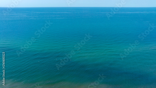 Wide panoramic view of the open sea with a calm blue and green color gradient, distant horizon and clear sky, tranquil ocean seascape from above