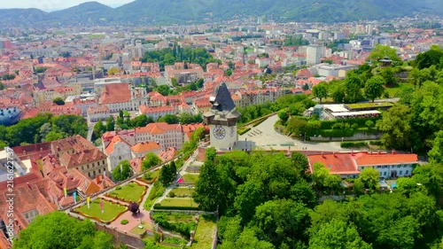 Graz, Austria. The Uhrturm clock tower with reversed hands and wooden gallery, Drone footage over terracotta rooftops and the historic city center. Drone footage, Departure of the camera