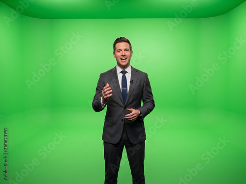 Professional news anchor in suit standing against a green screen background for chroma key.