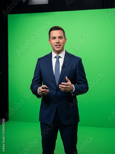 Professional male news anchor or business presenter standing in front of green screen.