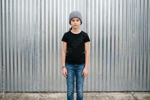 Young Girl in Black T-shirt and Beanie Standing Against Corrugated Metal Wall - Urban Style Portrait