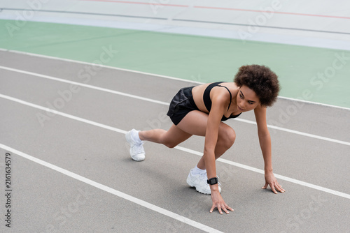 Fotografía Energetic young woman ready to sprint on an outdoor athletic track