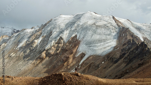 Drone photo of a woman near Molodezhny Peak overlooking Molodezhny Glacier near Almaty, Kazakhstan, in August, with the mountain range and Tuyuk-Su Glacier in the background.