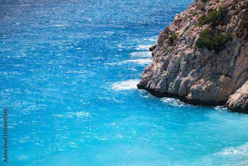 Elevated view of turquoise Mediterranean water meeting a rugged limestone headland dotted with shrubs along the Turkish coastline.