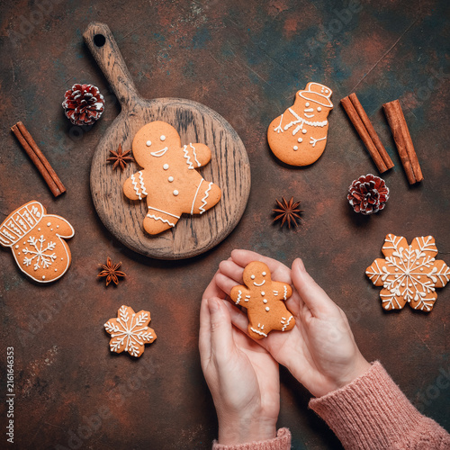 Gingerbread man in female hands on dark rustic background with Christmas decorations, top view, flat lay