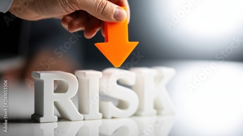 Hand holding orange arrow pointing down at white risk letters
